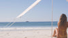beach shade with girl sitting under it in yellow bikini staring out to byron bay ocean under a sandstone colour beach tent