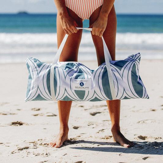 Blue and white beach tent bag in front of womans legs